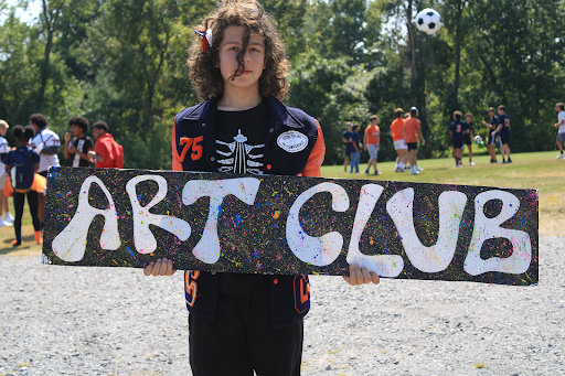 Freshman, Aaron Pinkston holding up the art club sign.
