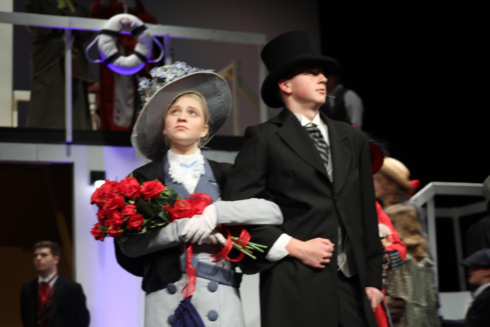 Two students playing first class passengers stand center stage.