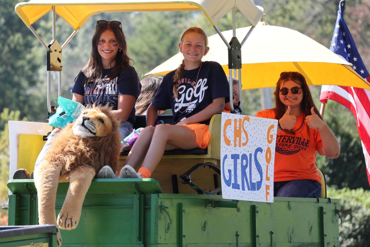 Senior Macie Clark, junior Hailey Halliday, and sophomore Merryn Elliott riding on the golf float while getting ready for the parade.
